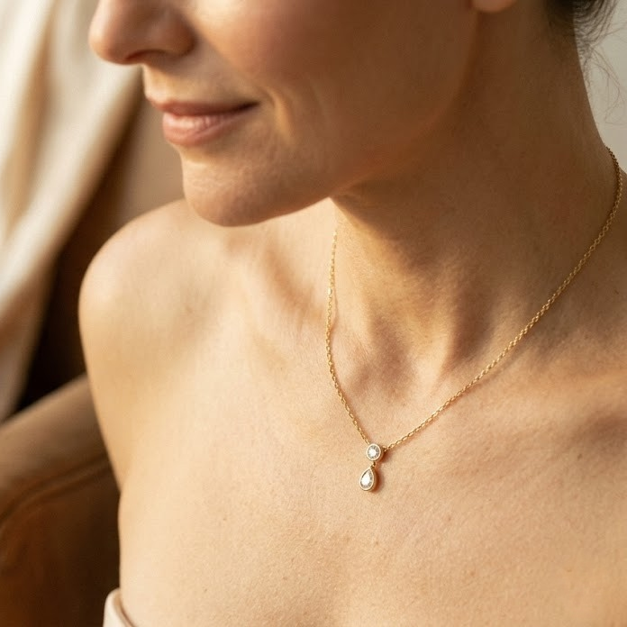 Close-up of a woman wearing a gold necklace with a pendant, bezel set with round and pear shape diamond. 